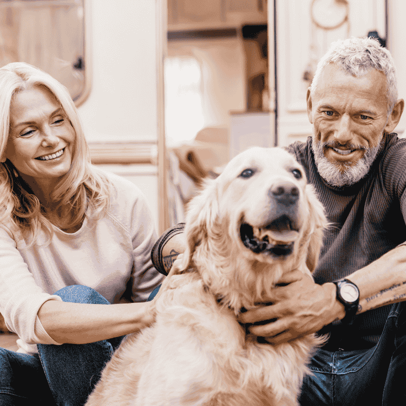 Couple in their 50s playing with their dog outside of their caravan