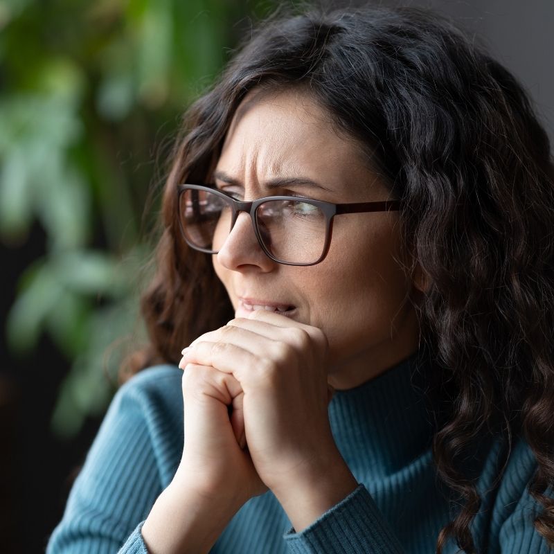 worried woman with glasses holding her hands